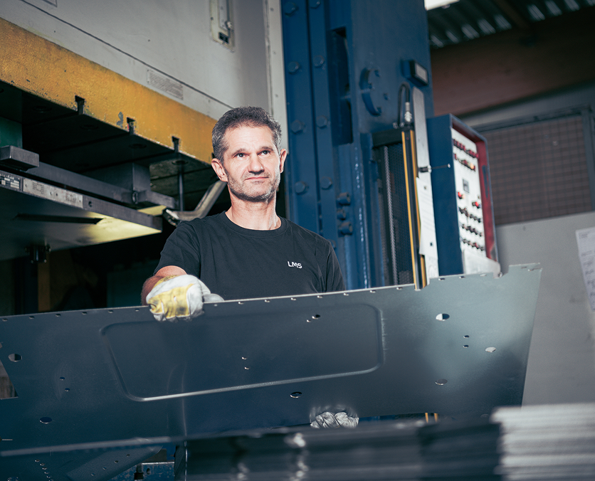 Produktsmitarbeiter entnimmt ein gepresstes Metallteil aus der Presse