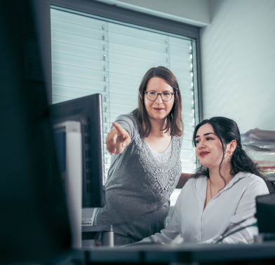 Ausbildungsleiter zeigt der Auszubildenden zur Industriekauffrau etwas am PC