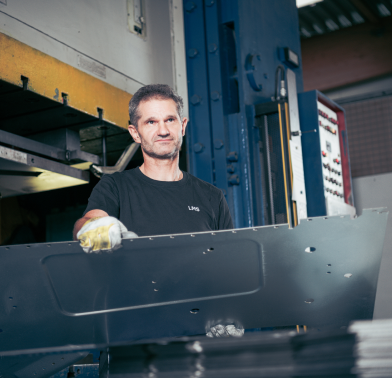 Produktionsmitarbeiter entnimmt ein gepresstes Metallteil aus der Presse