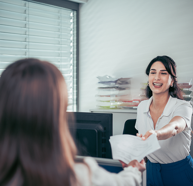 Auszubildende zur Industriekauffrau reicht ein Dokument an die Ausbildungsleiterin
